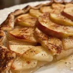 ['A close-up side view of a golden-brown apple galette, showcasing glistening apple slices.', 'A freshly baked apple galette on a rustic surface, highlighting its flaky crust and caramelized apple filling.', 'An iPhone 15 Pro photo of an apple galette, capturing the juicy apples and textured crust in detail.', 'A beautifully presented apple galette with a crispy crust and thinly sliced apples, ready to be served.']