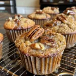 ['Close-up side view of caramel pecan muffins with a golden brown top and pecan pieces.', 'Juicy caramel pecan muffins showcasing a crumbly texture and glossy surface.', 'Side view of muffins with melted caramel glistening on top and chopped pecans scattered.', 'Delicious caramel pecan muffins displayed on a plate, highlighting their rich, moist texture.']