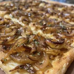 ['Close-up of a caramelized onion and fig flatbread with a golden crust.', 'Side view of a flatbread topped with caramelized onions, figs, and goat cheese.', 'Juicy flatbread featuring melted goat cheese and fresh rosemary on a wooden board.', 'Appetizing caramelized onion and fig flatbread displayed on a rustic table.']