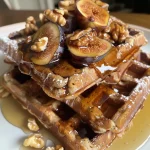 ['Close-up view of golden-brown waffles topped with figs and walnuts, displaying a rich texture.', 'A side perspective of delicious waffles garnished with sliced figs and walnut pieces, emphasizing their inviting look.', 'Textured waffles adorned with figs and walnuts, showcasing a warm and appetizing appearance.', 'Close-up shot of fluffy waffles featuring dried figs and walnuts, enhancing their visual appeal.']