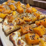 ['Close-up of a curried butternut squash flatbread topped with melted cheese and herbs.', 'Side view of a slice of flatbread with butternut squash, cheese, and curry seasoning.', 'Detailed shot of curried butternut squash flatbread showcasing the vibrant colors of the ingredients.', 'Slice of naan bread loaded with roasted butternut squash and cheese in a rich curry flavor.']