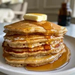 ['Close-up side view of fluffy, golden-brown Double Chai Spiced Pancakes stacked on a plate.', 'Juicy and delicious Double Chai Spiced Pancakes with a light dusting of powdered sugar on top.', 'Side view of warm Double Chai Spiced Pancakes drizzled with syrup, showcasing their spiced texture.', 'A stack of moist Double Chai Spiced Pancakes garnished with a cinnamon stick and a sprinkle of spices.']