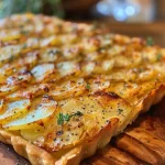 ['Close-up view of a delicious potato tart topped with thyme and lemon zest.', 'Juicy potato tart with a golden crust, fresh thyme, and garlic, seen from the side.', 'Side angle of an easy potato tart showcasing layers of potatoes and herbs.', 'Detailed shot of a savory potato tart revealing a flaky pastry filled with lemon and thyme.']