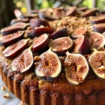 ['Close-up side view of a fresh fig cake with a crumb topping.', 'Juicy fig cake slice showcasing crumb topping and fresh figs.', 'Side profile of a freshly baked fig cake garnished with chopped pecans.', 'Detailed view of a moist fresh fig cake highlighting its crumbly texture.']