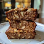 ['A side view of a loaf of High Protein Cinnamon Apple Banana Bread with visible chunks of apples and bananas.', 'Close-up image of freshly baked High Protein Cinnamon Apple Banana Bread showcasing its moist texture and spices.', 'A delicious slice of High Protein Cinnamon Apple Banana Bread revealing a soft interior and apple pieces.', 'Side perspective of golden-brown High Protein Cinnamon Apple Banana Bread on a wooden cutting board.']
