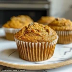 ['Close-up of a golden-brown pumpkin muffin with a moist texture.', 'Side view of high-protein pumpkin muffins showcasing their fluffy tops.', 'Delicious pumpkin muffins with a sprinkle of cinnamon on top.', 'Juicy high-protein pumpkin muffins arranged on a rustic wooden table.']