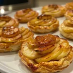 ['Close-up view of mini cinnamon apple tarts with golden puff pastry and cinnamon-dusted apple slices.', 'Side view of freshly baked mini cinnamon apple tarts showcasing apple filling and flaky crust.', 'Juicy mini cinnamon apple tarts arranged on a plate, highlighting ingredients like apples and cinnamon.', 'Detailed photo of mini tarts filled with apple slices, glistening with apricot jelly glaze.']