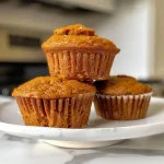 ['Close-up view of a moist pumpkin honey muffin with a golden brown crust and visible pecans.', 'Side angle of a freshly baked pumpkin honey muffin, showcasing its fluffy texture and shiny sugar topping.', 'Delicious pumpkin honey muffin displayed with a soft, crumbly top and specks of cinnamon and nuts.', 'Juicy pumpkin honey muffin on a plate, highlighting its rich color and crispy outer layer.']