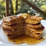 ['Golden-brown pumpkin spice pancakes stacked on a plate, with syrup drizzling on top.', 'Fluffy pumpkin spice pancakes served with a dollop of whipped cream and a dusting of cinnamon.', 'A close-up view of pumpkin spice pancakes showcasing their texture and a slice of pumpkin beside them.', 'Delicious pumpkin spice pancakes topped with maple syrup and sprinkled with chopped nuts.']