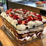 ['A close-up view of a colorful trifle displayed in a tray, showcasing layers of berries and cream.', 'Side view of a delectable trifle in a tray, with vibrant layers of jelly, strawberries, and whipped cream.', 'A beautifully arranged trifle in a tray, highlighting mixed berries and cake layers topped with cream.', 'A tempting trifle in a tray featuring colorful layers of jelly, cake, and fresh strawberries.']