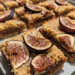 ['Close-up of fudgy blondies with ripe fig slices on a wooden surface.', 'Side view of moist blondies topped with quartered figs, showing rich texture.', 'Delicious-looking blondies featuring fig pieces, captured on an iPhone.', 'Tasty fig blondies with a glossy finish displayed on a rustic table.']